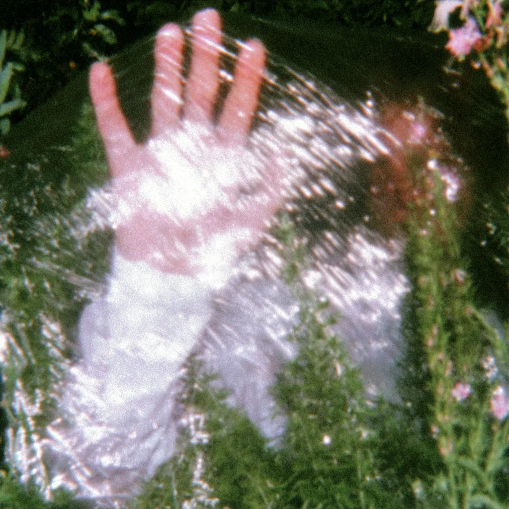 a hand reaching through a sheet of transparent plastic wrap, surrounded by green foliage. bright white, glowing, soft colors, ethereal, tiny exotic pink flowers in the background, sparkles